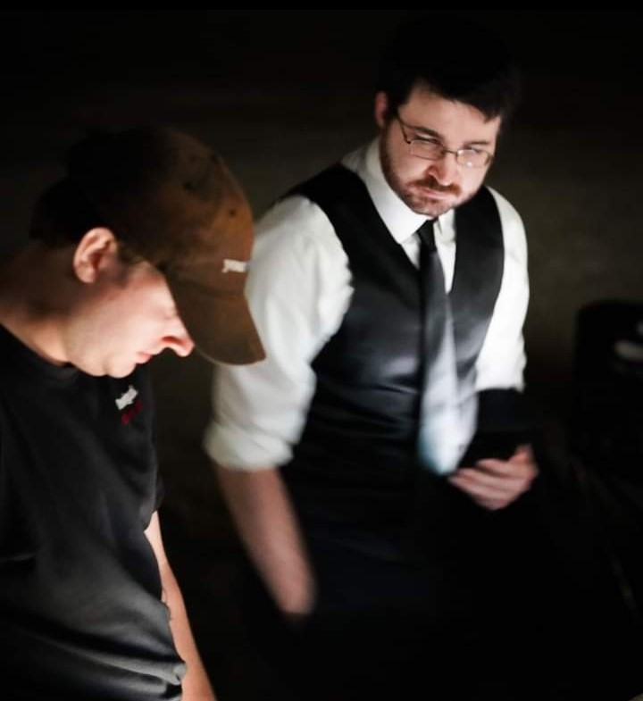 Andrew Lauck in character on a film set looking at a script with the director of photography.