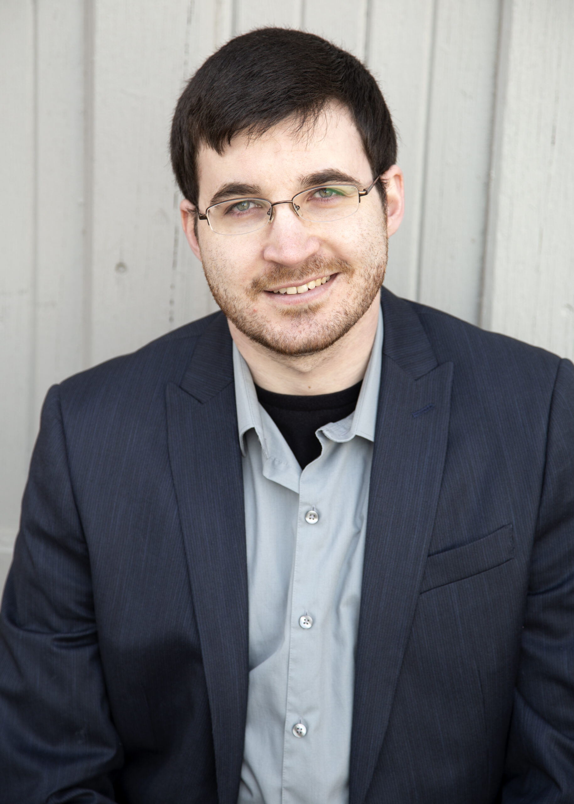 Andrew Lauck, the author, posing for his headshot in a button-up shirt and suit jacket.